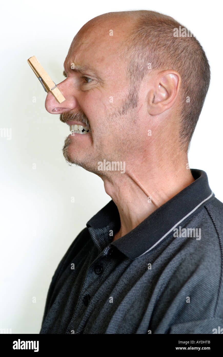 Profile of grimacing man with a clothes pin on large nose to block a