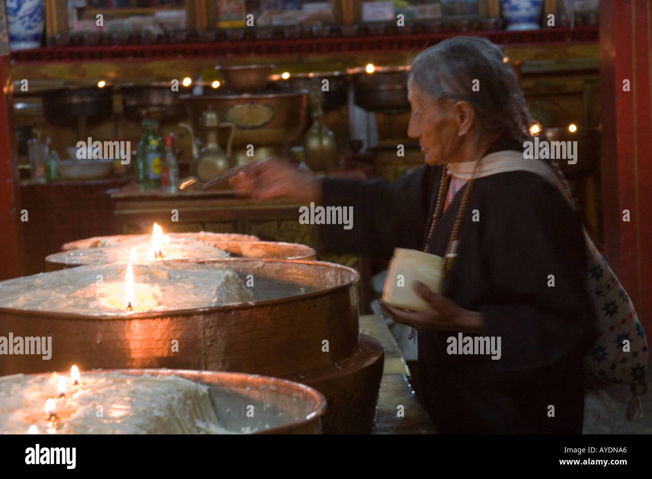 Tibetan pilgrim woman tendng the yak butter candles in a monastary in