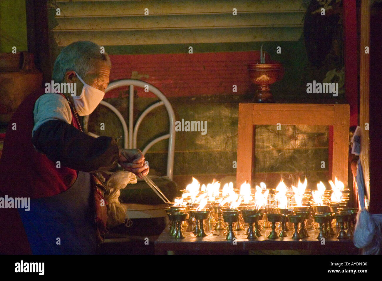 Tibetan monk tending to yak butter candles on a shrine in a small