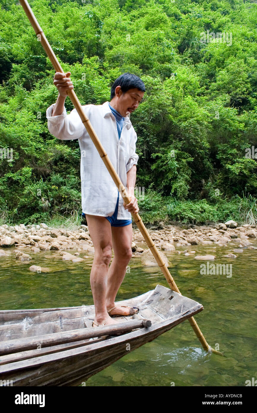 Chinese fisherman using a bamboo pole to push his peapod boat on