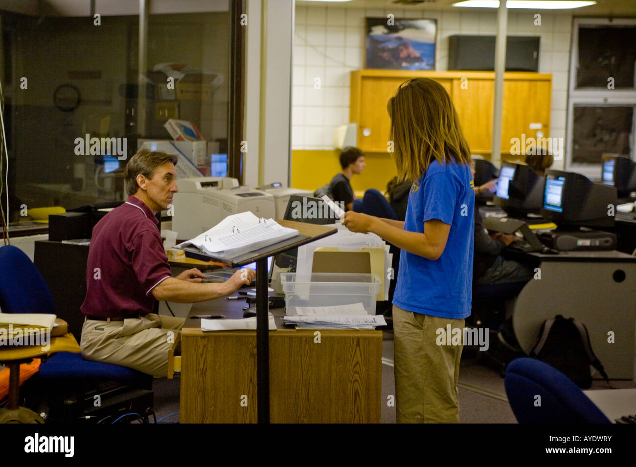 A long haired high school student in San Clemente California talks to his teacher during touch typing computer science class Stock Photo