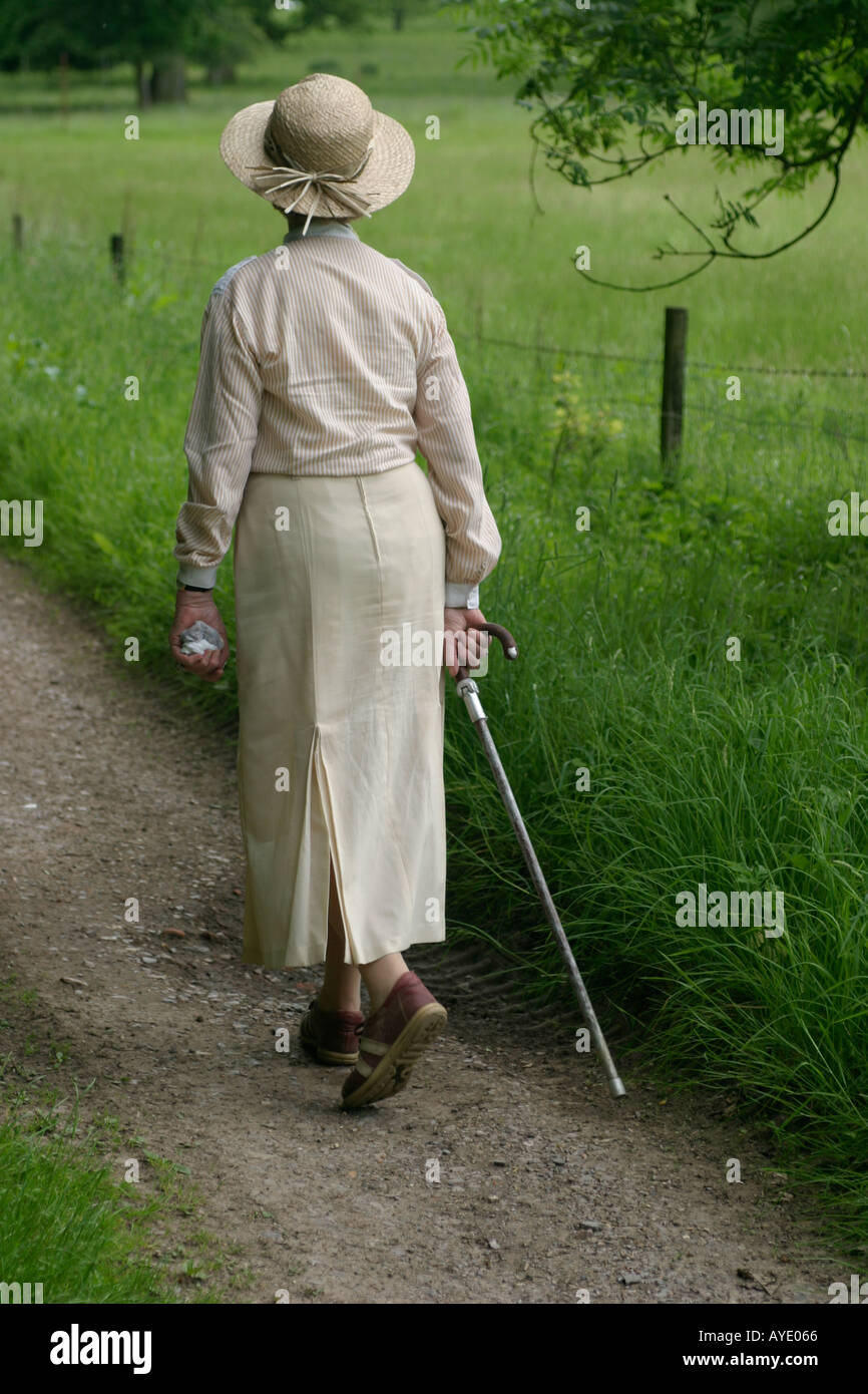 English woman aged seventies walks in the English countryside with walking stick Stock Photo