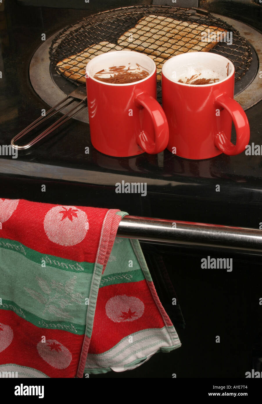 Toasting bread on the hot plate of an Aga with two red mugs of hot