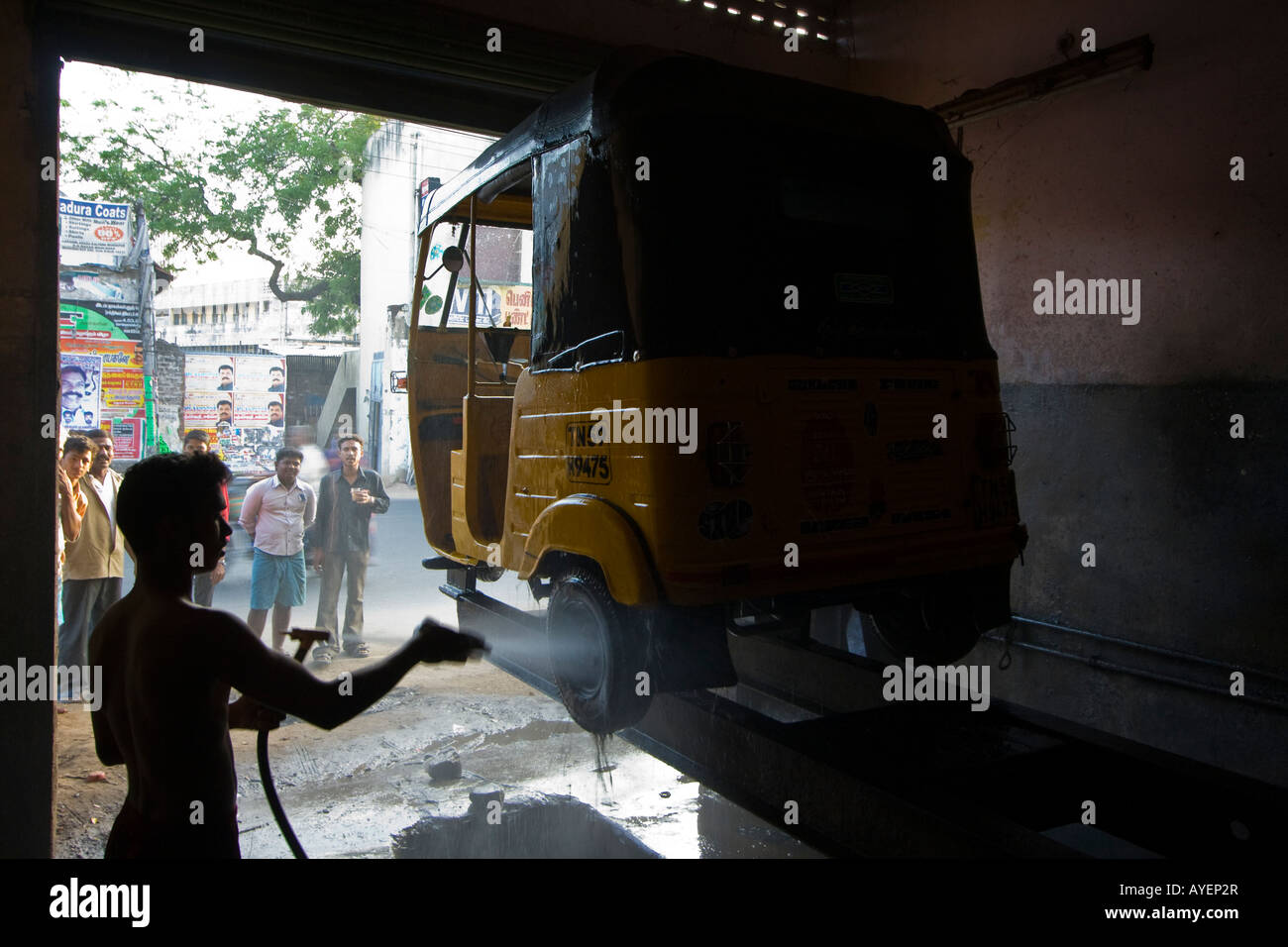 Young Indian Man in a Repair Shop Washing an Auto Rickshaw in Madurai