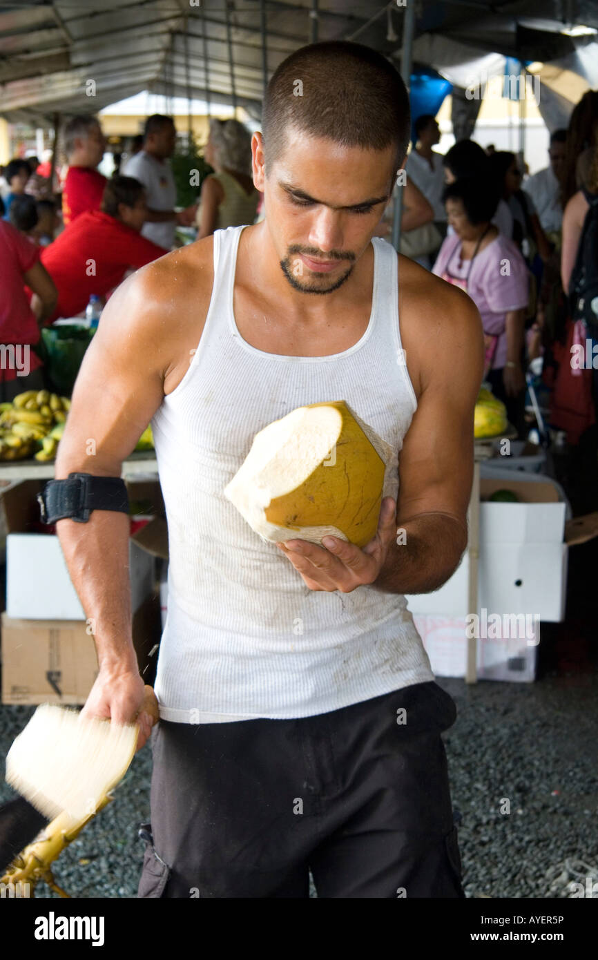Hawaiian man cutting the husk off of a coconut at a market in Hilo on