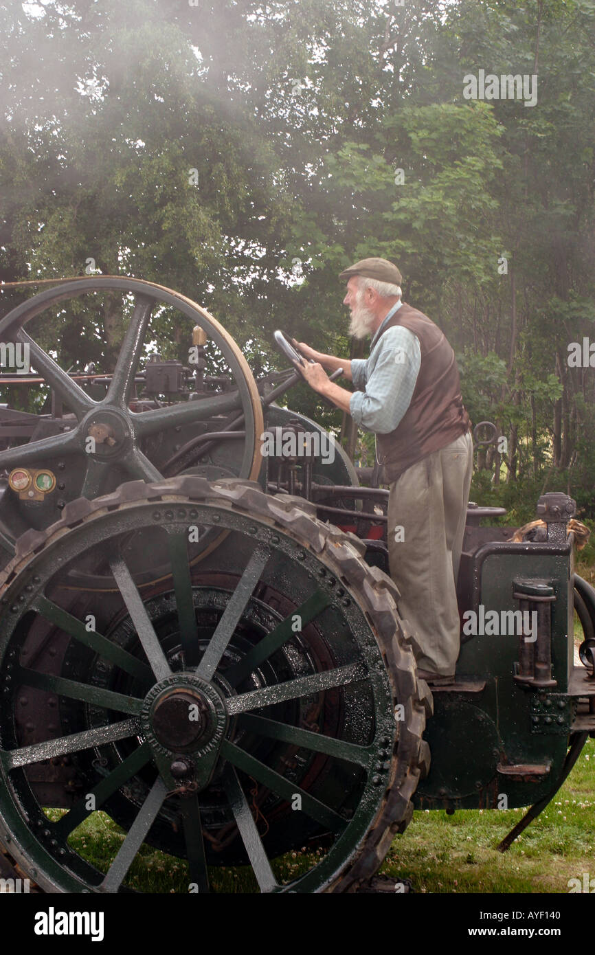 Beared old man controlling stationary traction engine with belt driven power take off to threshing machine Stock Photo