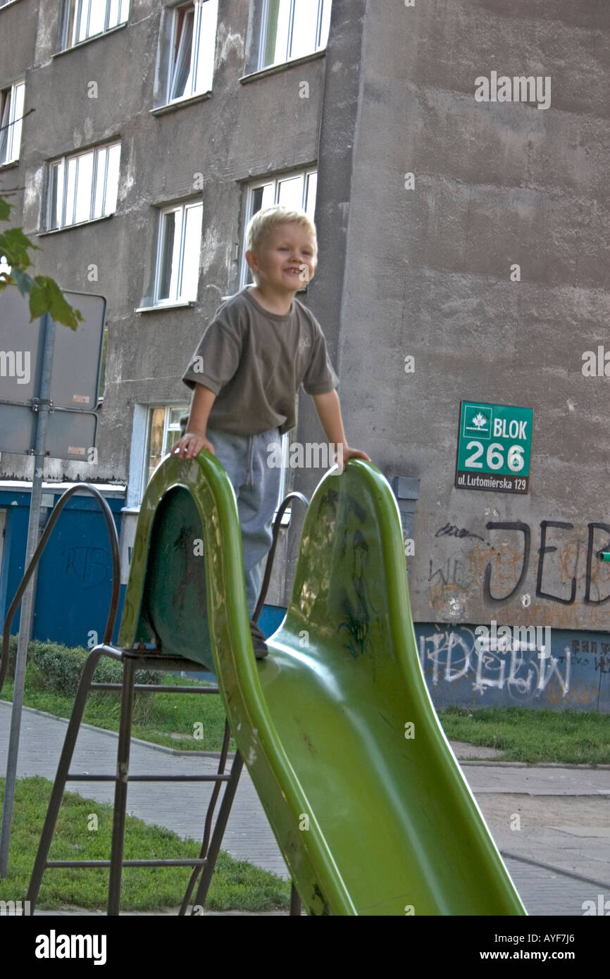 Boy age 3 playing on park slide in front of his Communist built Blok home. Lodz Central Poland Stock Photo