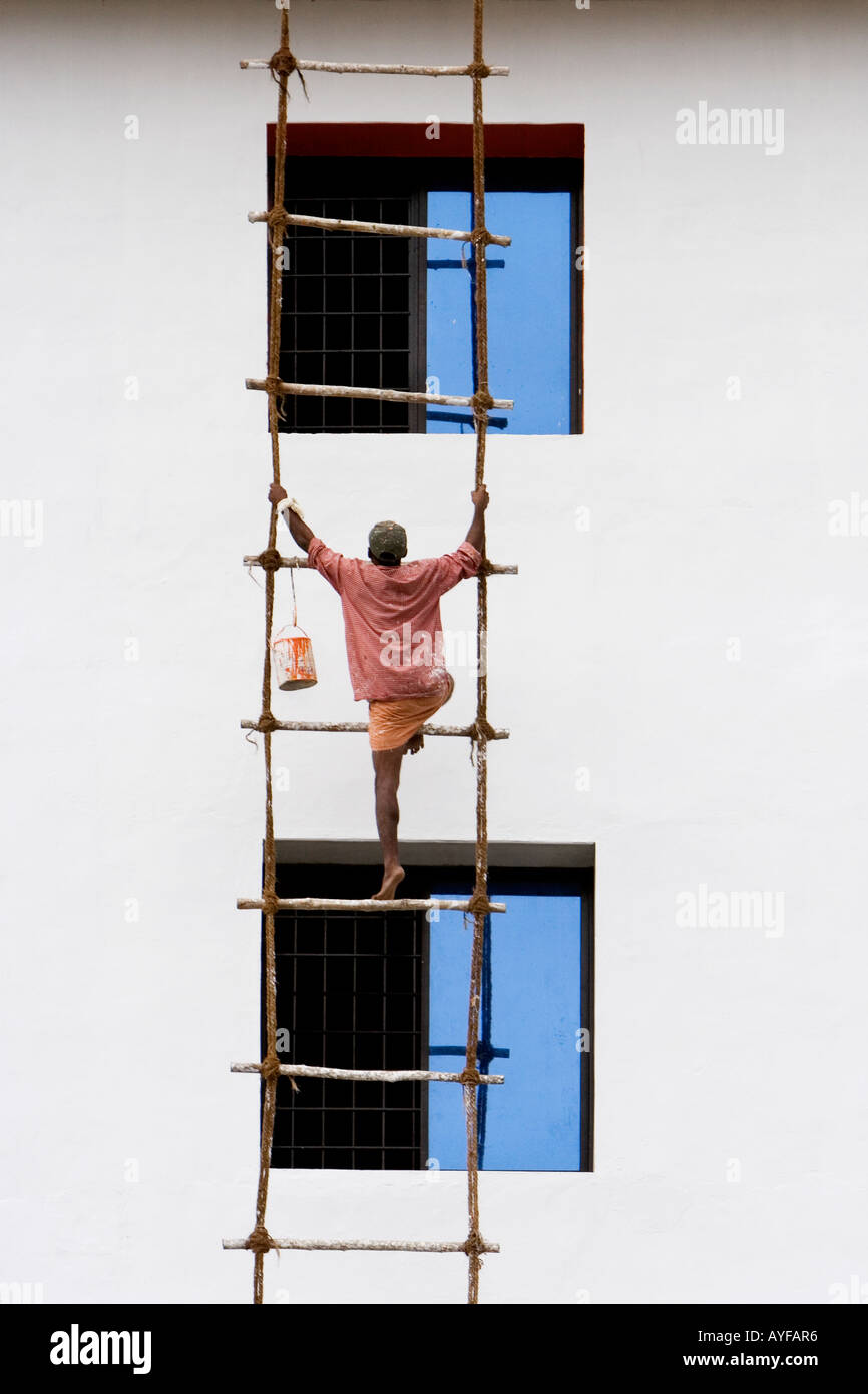 Indian man climbing a rope ladder to paint the exterior of a building