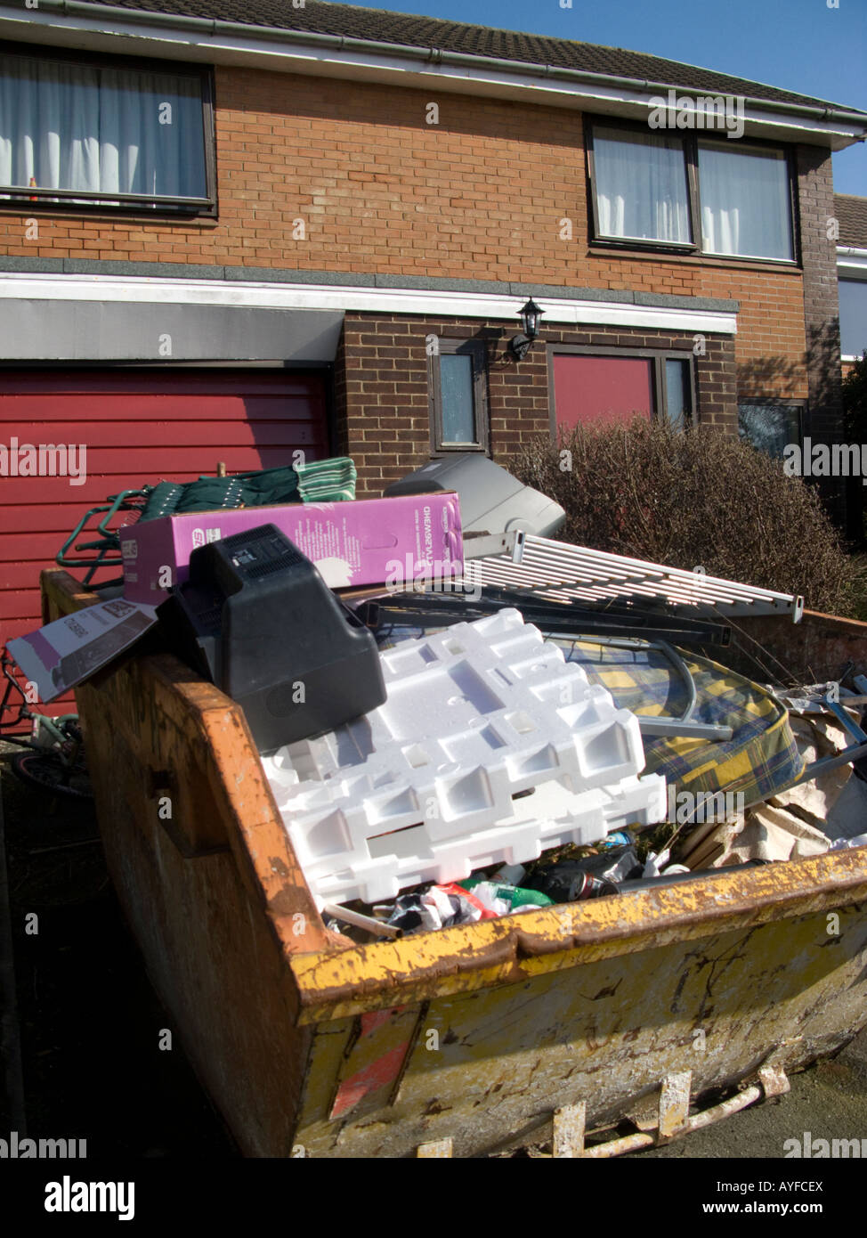 A Skip full of household junk and rubbish outside house on suburban