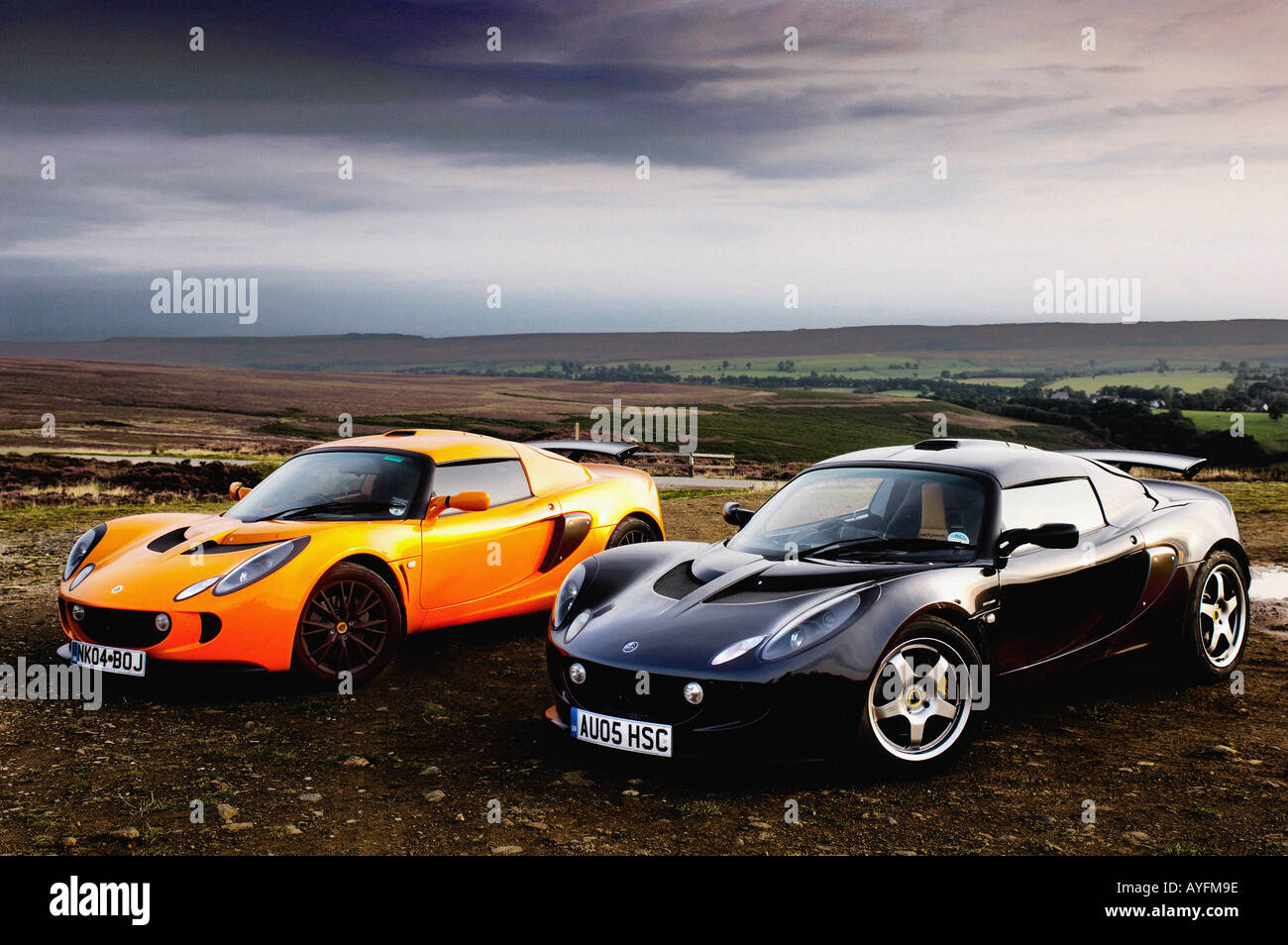 Two Lotus Exige cars, one orange and one black parked side by side with the dramatic scenery of the North Yorkshire Moors in the distance. Stock Photo