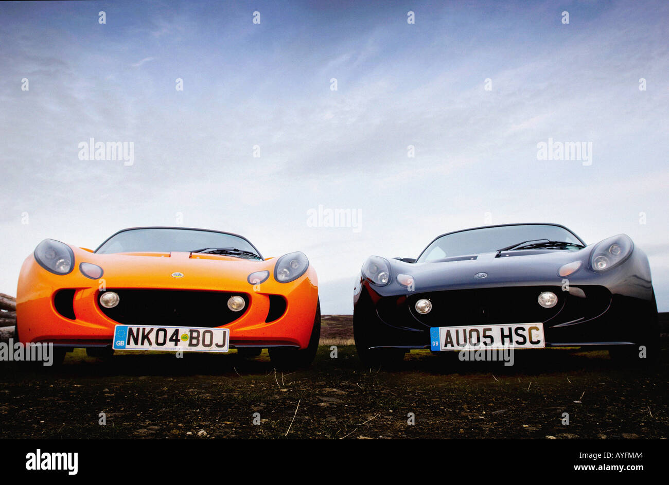 Two Lotus Exige cars, one orange and one black parked side by side with the dramatic scenery of the North Yorkshire Moors in the distance. Stock Photo