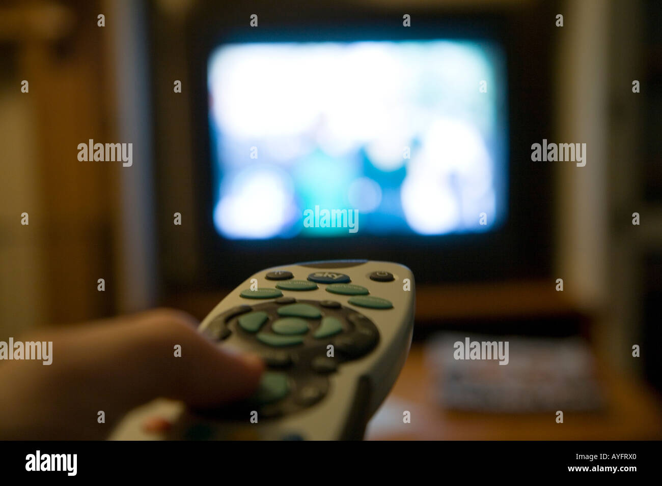 Man's left hand operating Sky remote control with television set in the background Stock Photo