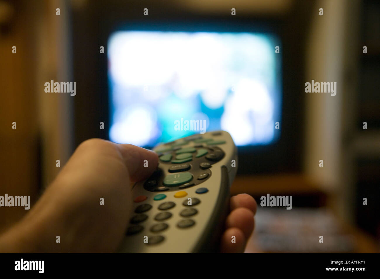 Man's left hand operating Sky remote control with television set in the background Stock Photo