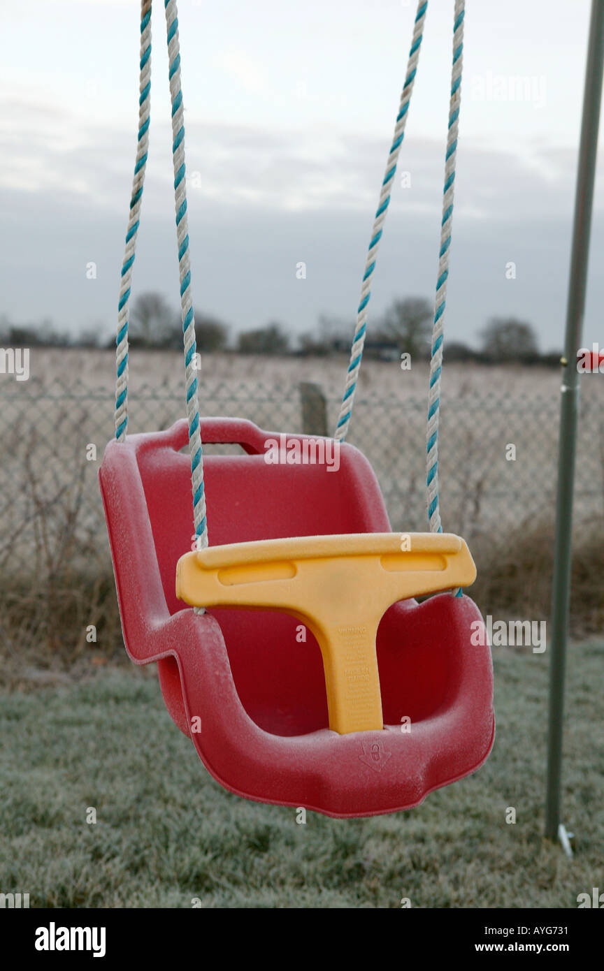 childs red swing seat idle in the early morming frost with landscape in the background Stock Photo