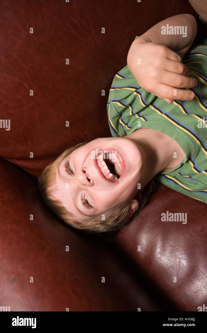 five year old boy laughing on sofa at home Stock Photo