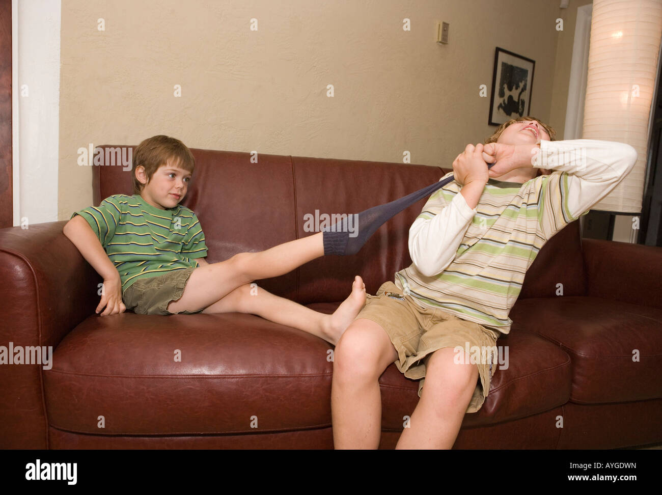 older brother pulling sock off of younger brother's foot at home on sofa  Stock Photo - Alamy