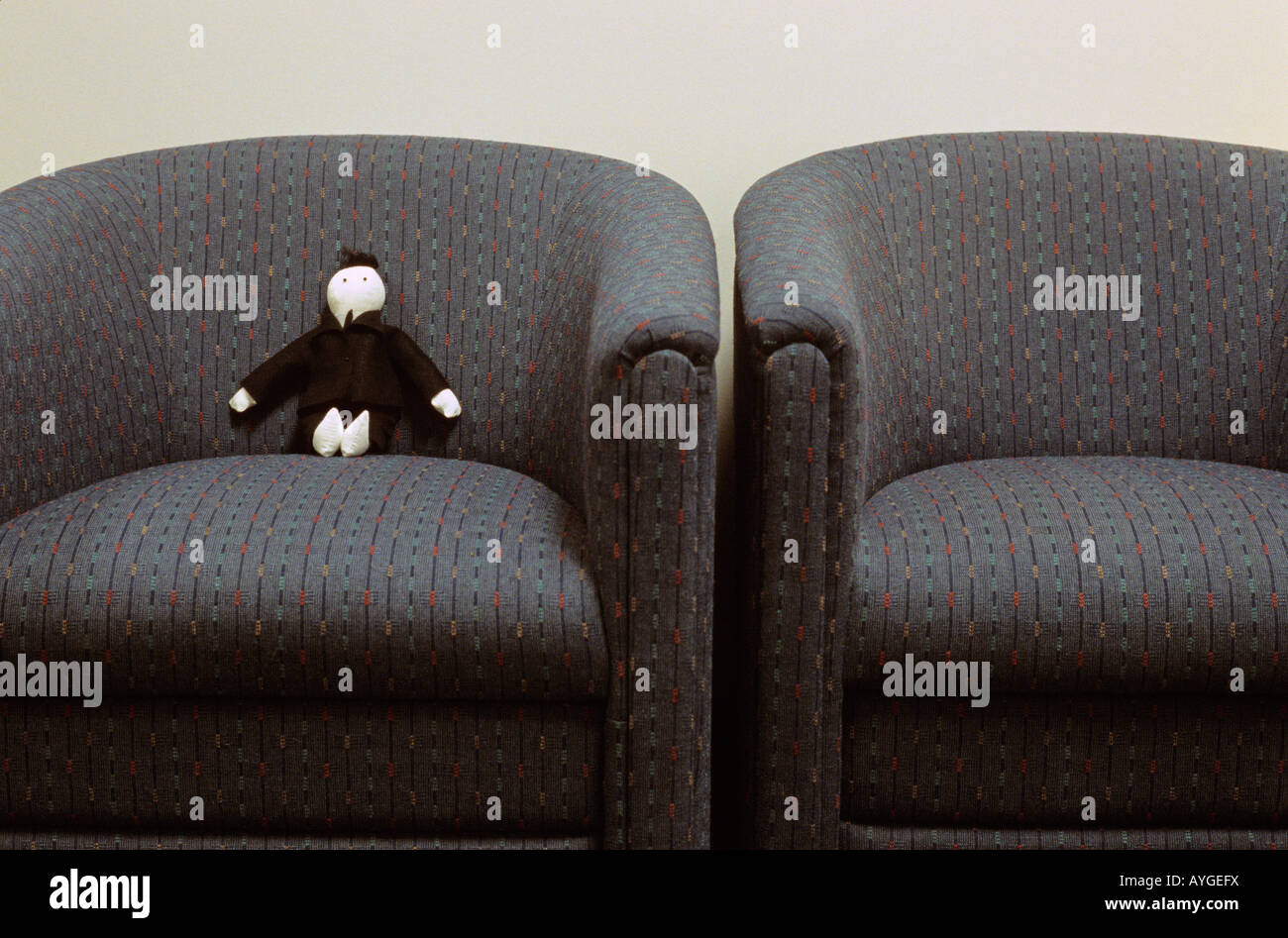 Voodoo doll sitting in chair in office lobby dressed as a business man in a black suit and blue tie Stock Photo