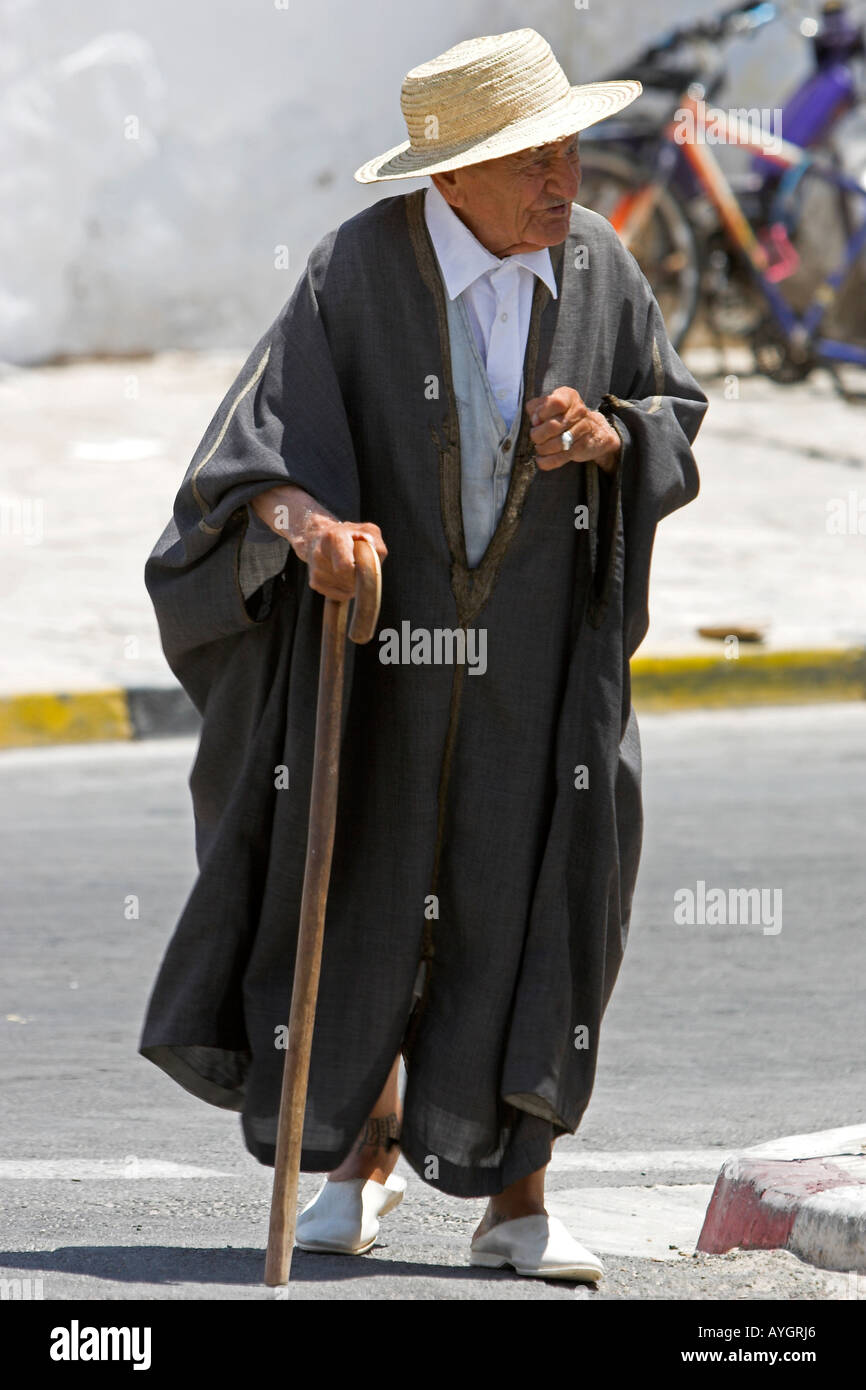 Old Berber man in traditional woollen cloak and straw hat walks with stick in street Matmata Tunisia Stock Photo