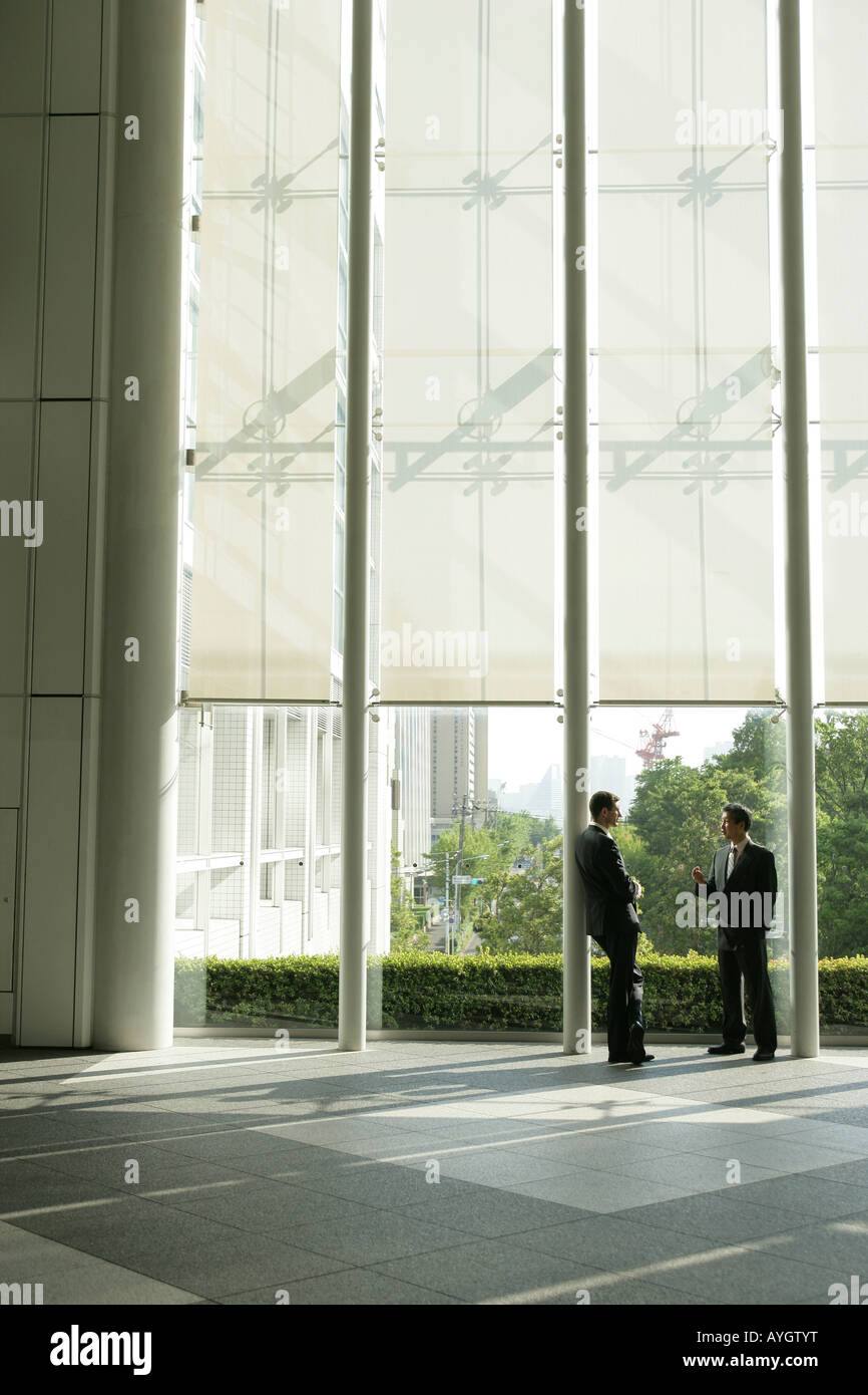 Two businessmen talking in office building's lobby Stock Photo - Alamy