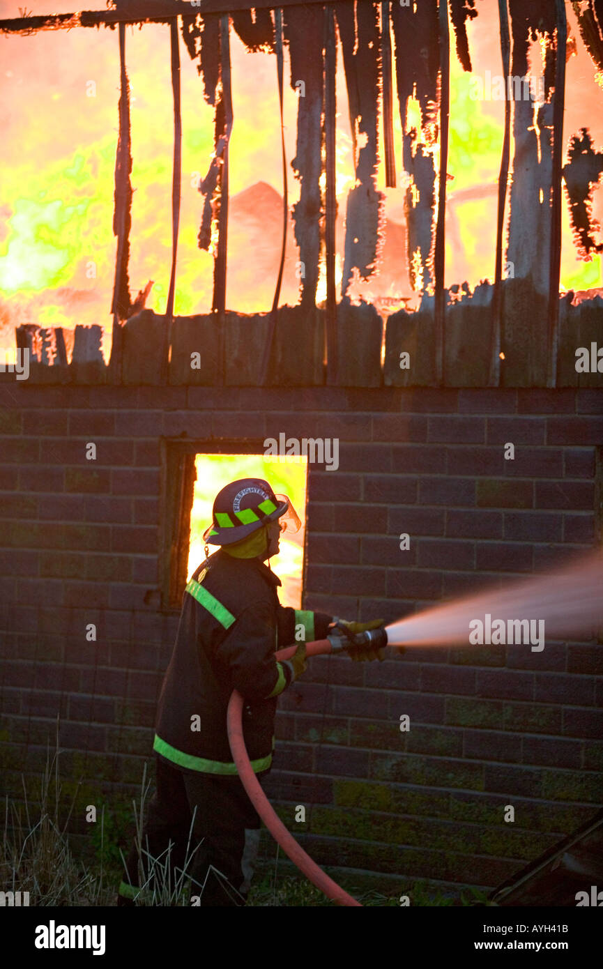 Firefighter attacks burning building with fire hose Stock Photo