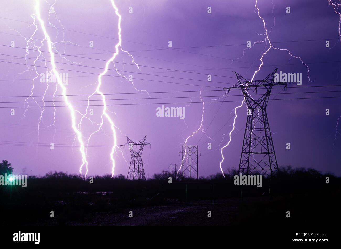 Large lightning bolts strike near power lines during a summer monsoon storm with purple sky in Vail, Arizona, United States. Stock Photo