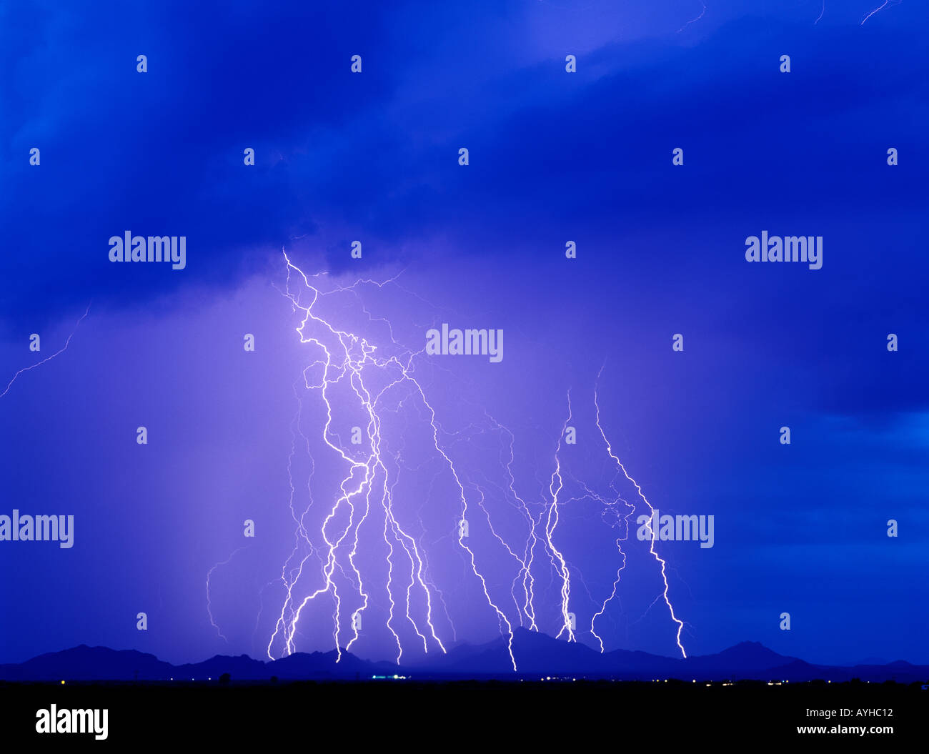 Lightning bolts strike a mountain range from a brilliant blue sky during a summer monsoon storm in Southern Arizona, USA. Stock Photo