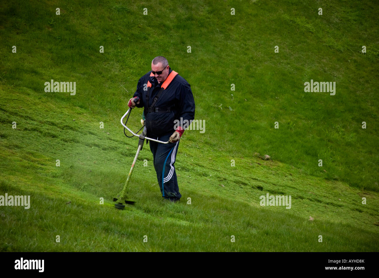 Man strimming grass slope with strimmer machine Stock Photo