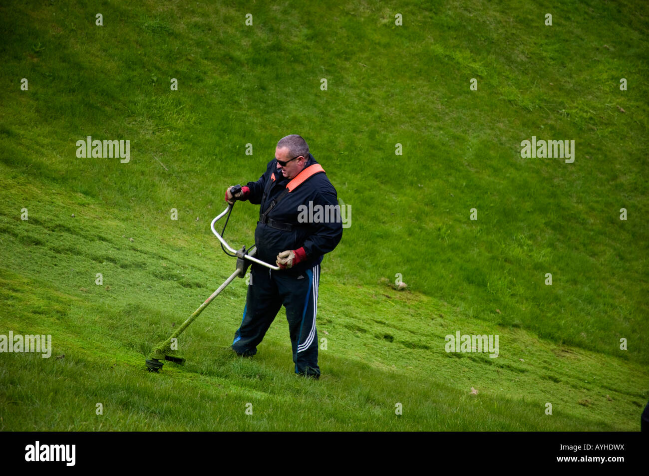 Man strimming grass slope with strimmer machine Stock Photo