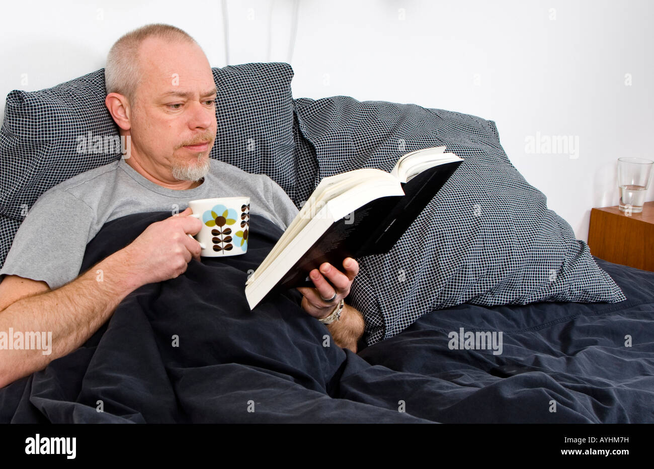 Man in bed reading a book Stock Photo