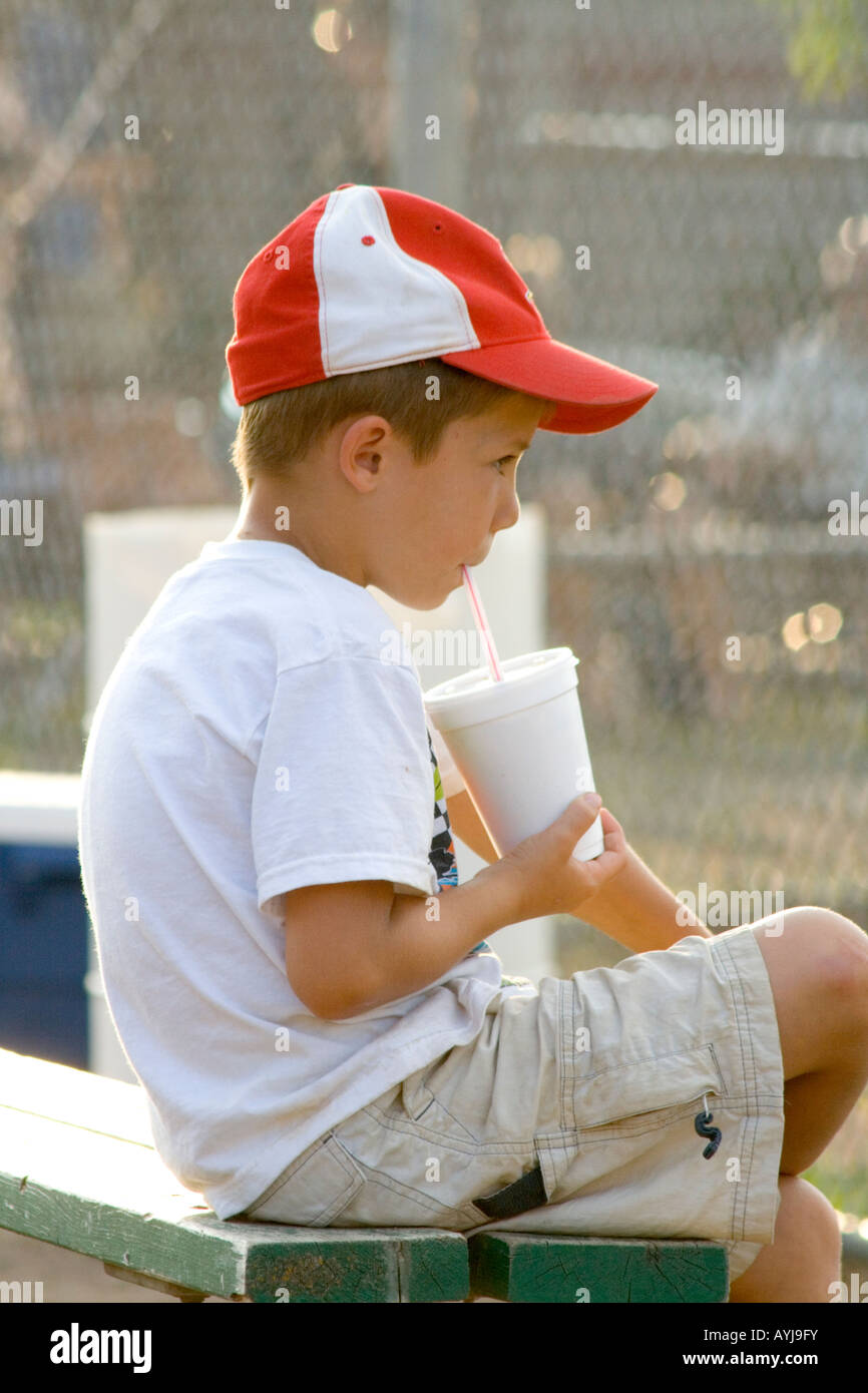 Young boy age 6 watching baseball game while sipping drink through