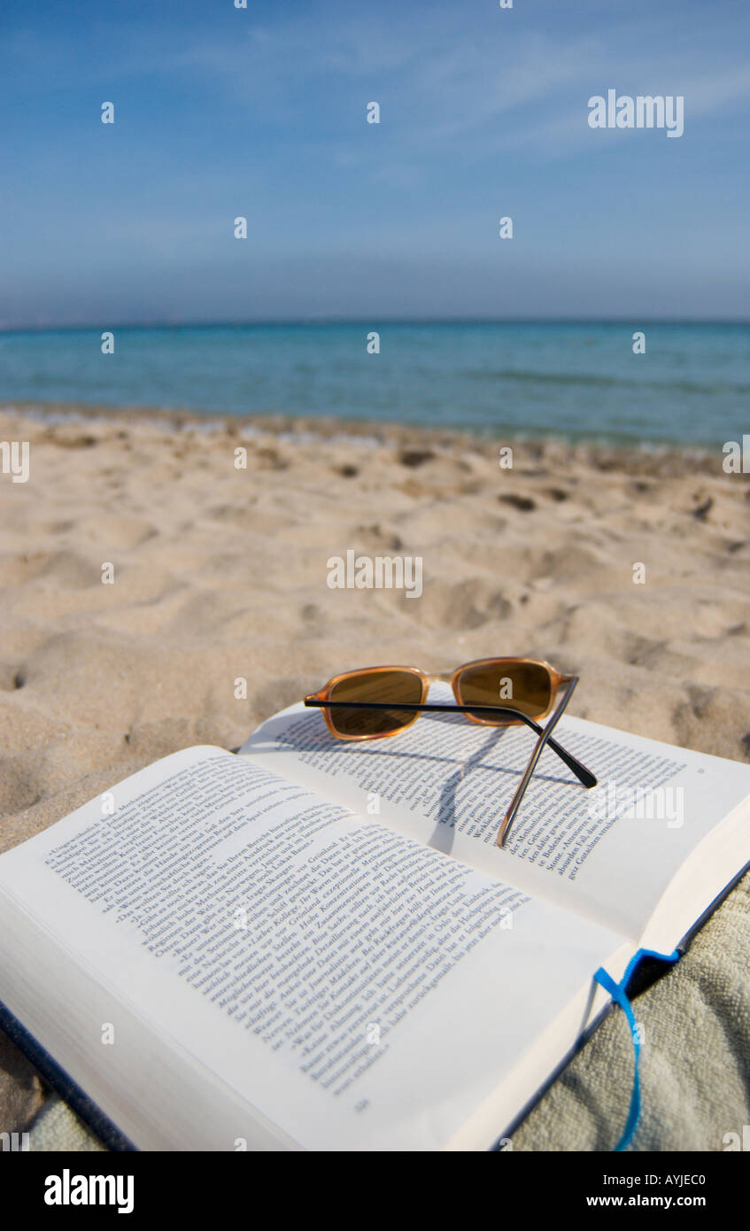 open book and sunglasses in the sand on the beach Stock Photo