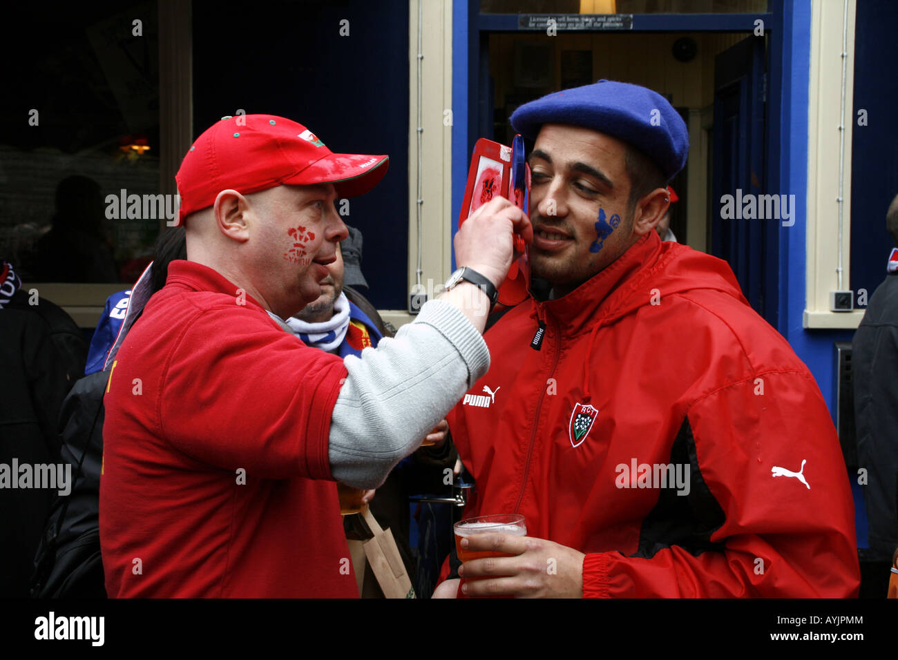 Welsh fan applies face paint to a French rugby supporter in Cardiff for the 6 Nations game Wales v France, 2008 Stock Photo