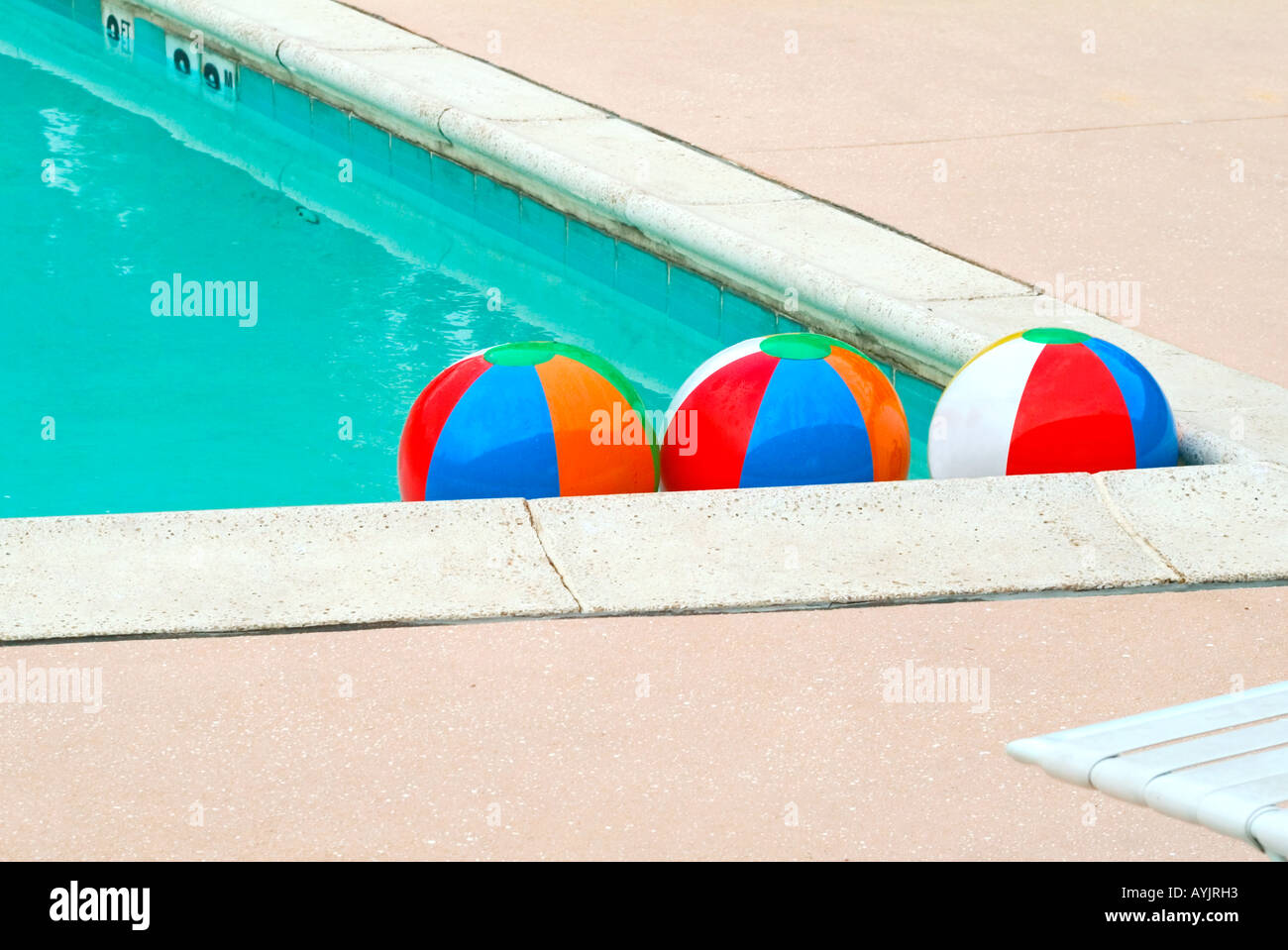 Three colorful beach balls in the corner of the pool illustrating the concept of how people gravitate together Stock Photo
