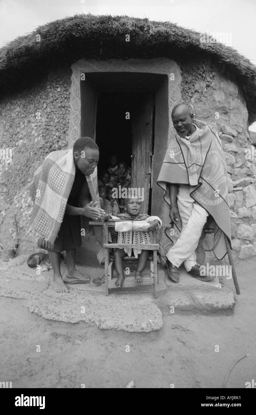 B/W of a family with their disabled young child outside their rondavel in a remote area with little access to healthcare. Maseru District, Lesotho Stock Photo