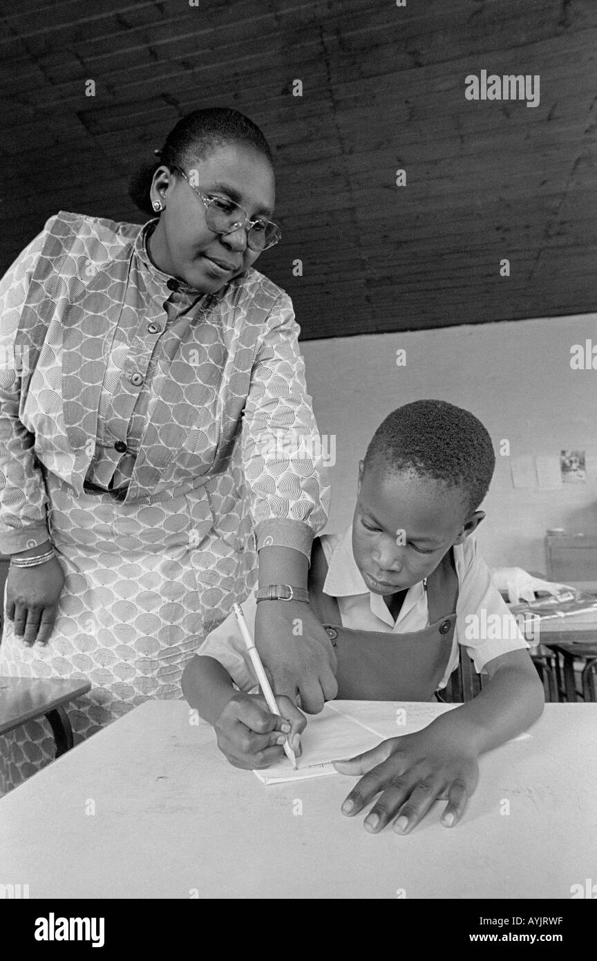 B/W of a teacher helping a young boy to write at a rural junior school. Lesotho Stock Photo
