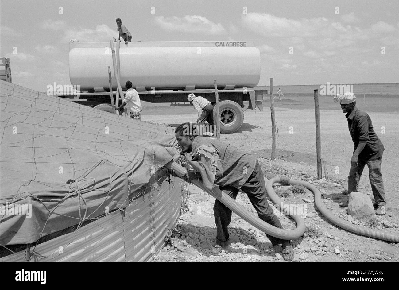 B/W of men filling a storage tank from a water tanker at a refugee camp for displaced Somalis on the border. Kebrebeyah, Ethiopia, Africa Stock Photo