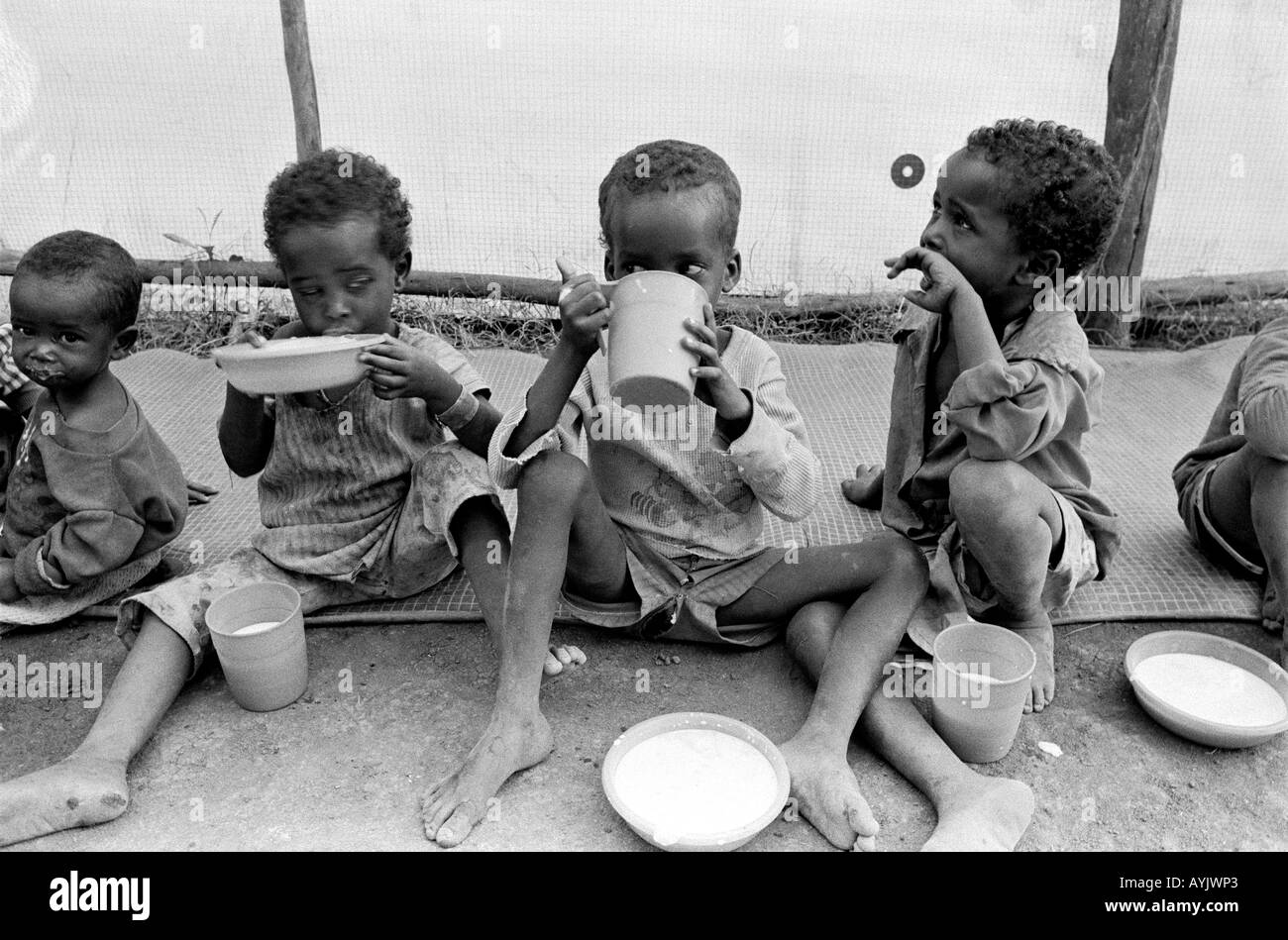 B/W of Somali refugee children eating at a feeding center in a refugee ...