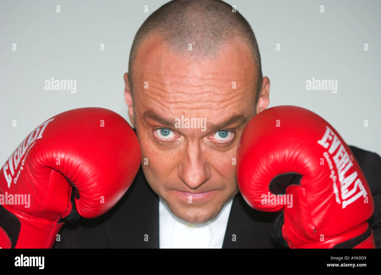 balding man in his 40s wearing a black suit is raising red boxing gloves Stock Photo