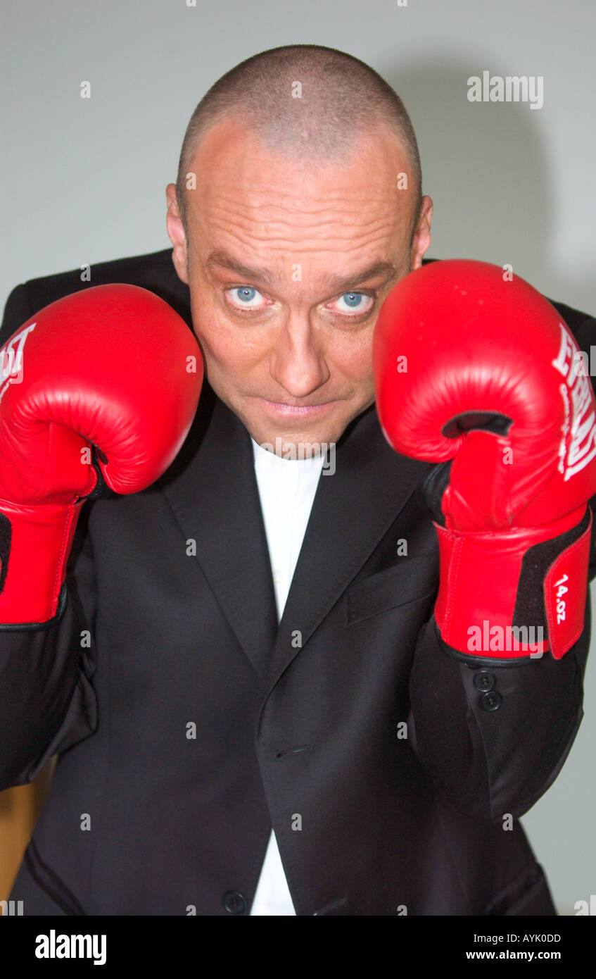 balding man in his 40s wearing a black suit is raising red boxing gloves Stock Photo