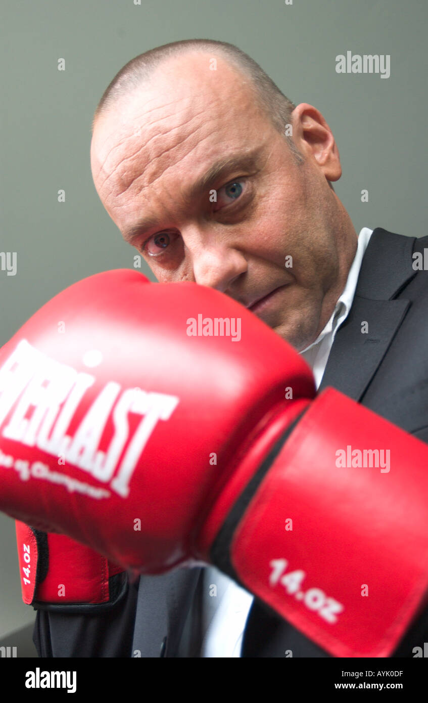 balding man in his 40s wearing a black suit is raising red boxing gloves Stock Photo