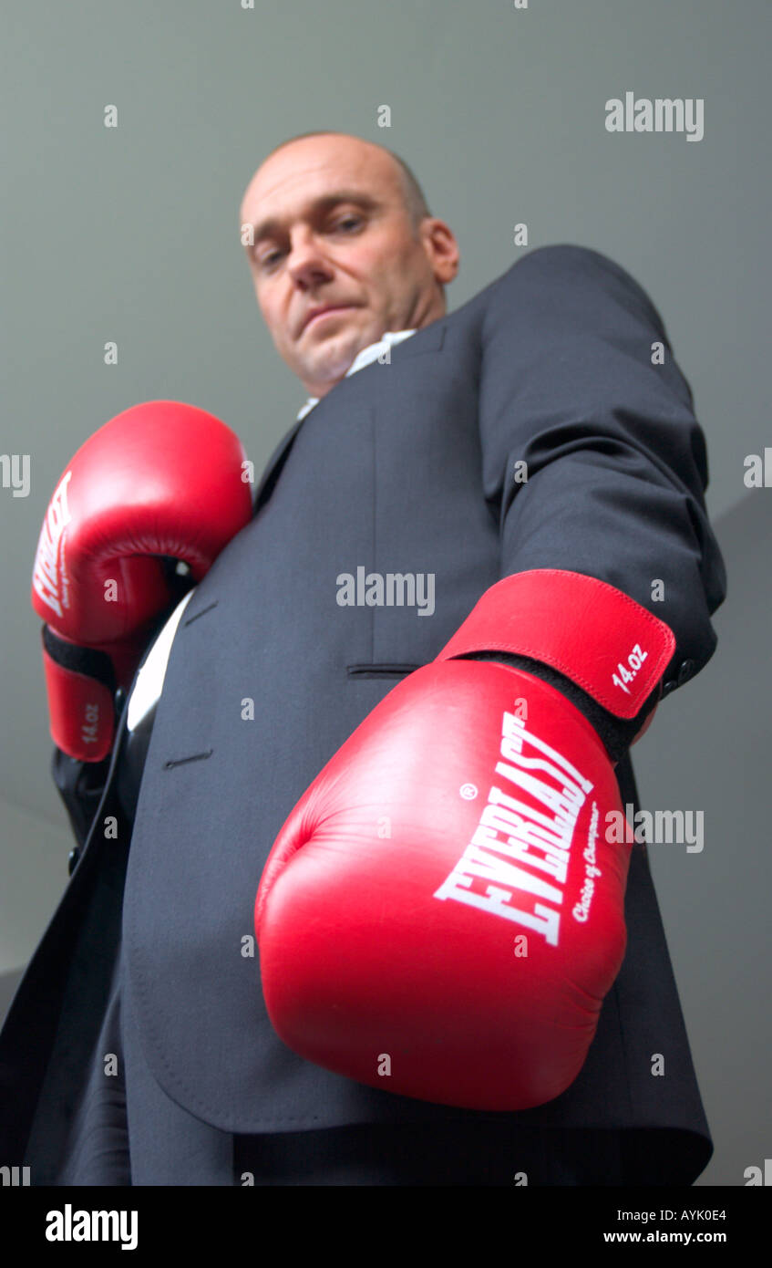 bald business man wearing boxing gloves stares down into camera Stock Photo