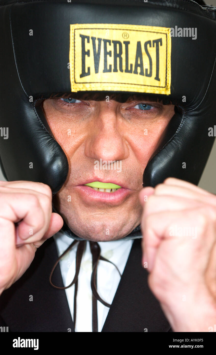 businessman in his forties wearing head protector and mouthguard is raising his fists close to his face striking a boxing pose Stock Photo