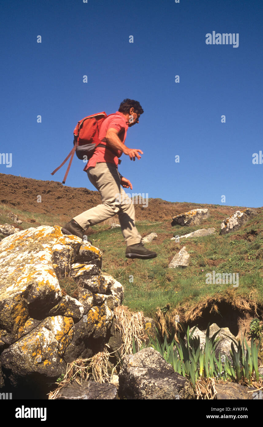 Retired man scrambling and jumping over rocks in Cornwall, UK Stock Photo