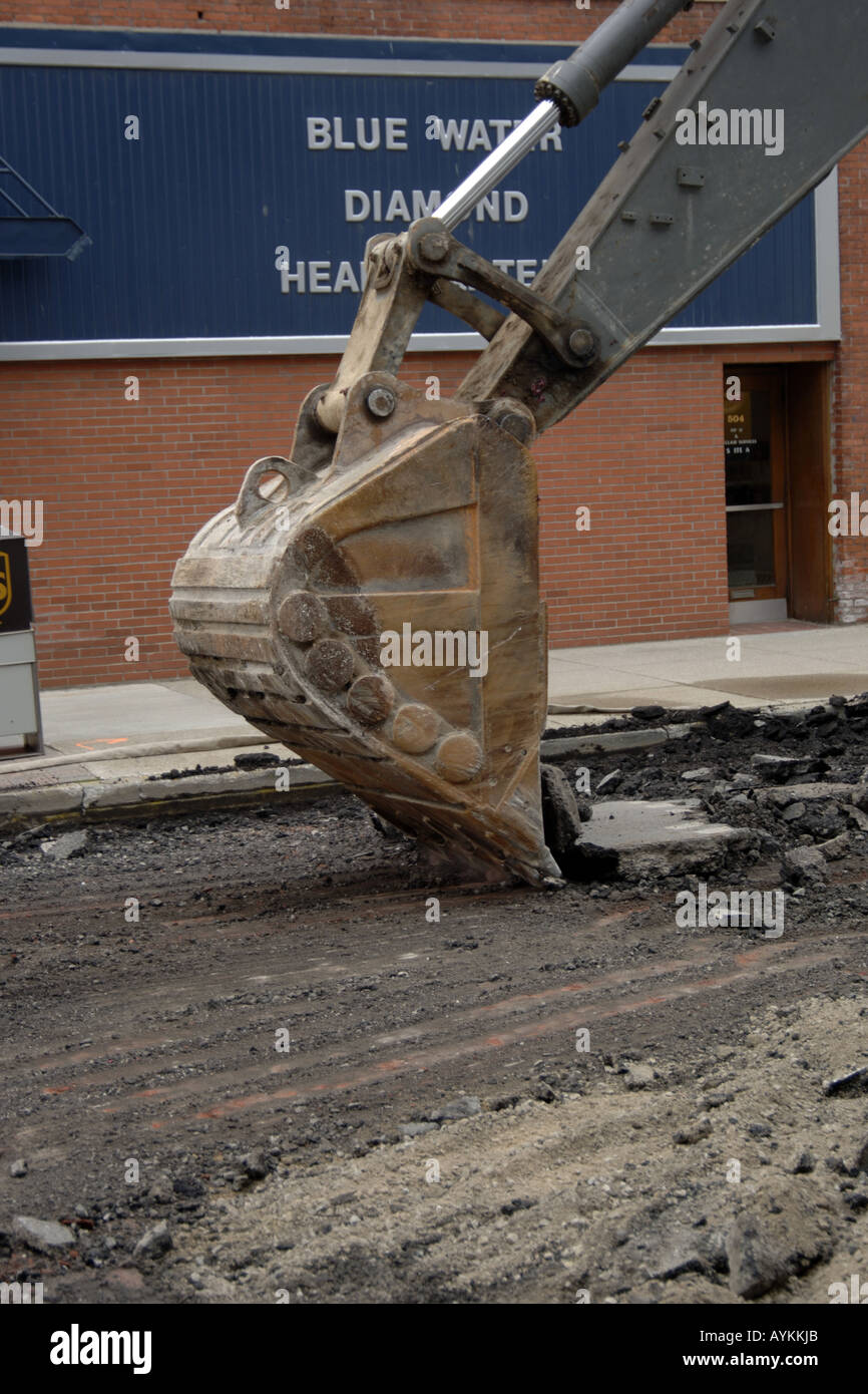 Specific image of a bucket on a backhoe excavating machine being used to remove asphelt from a road Stock Photo