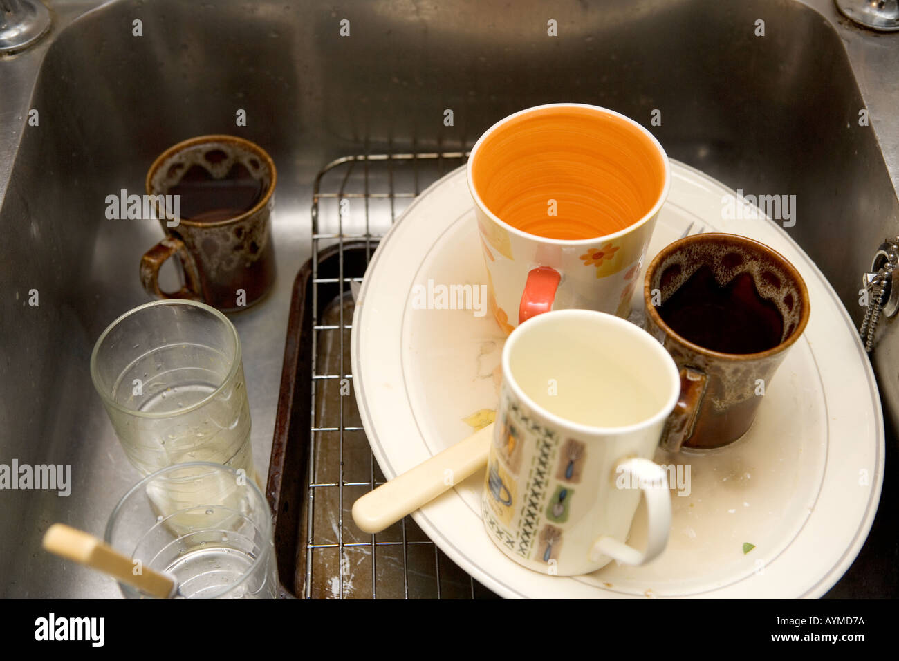 Dirty washing up including cups and plates in a stainless steel sink Stock Photo