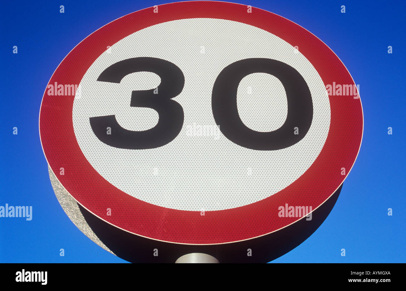 Close up of circular speed limit road sign stating 30 against blue sky ...