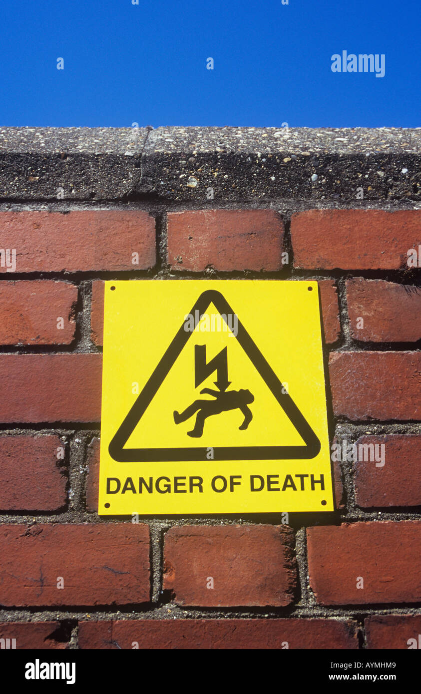 Old orange brick wall with concrete lintel under blue sky with sign with iconic electrocuted man and words Danger of death Stock Photo