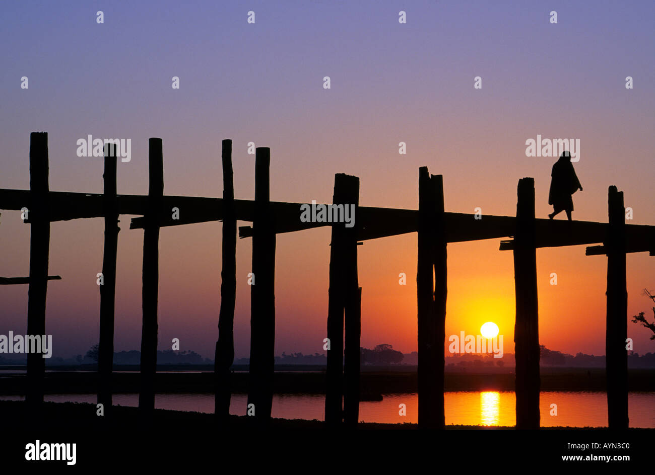 U Bein Bridge Myanmar Burma. Monk crossing U Bein's Bridge on Taungthaman lake at Amarapura near Mandalay at sunset. World longest teak structure. Stock Photo