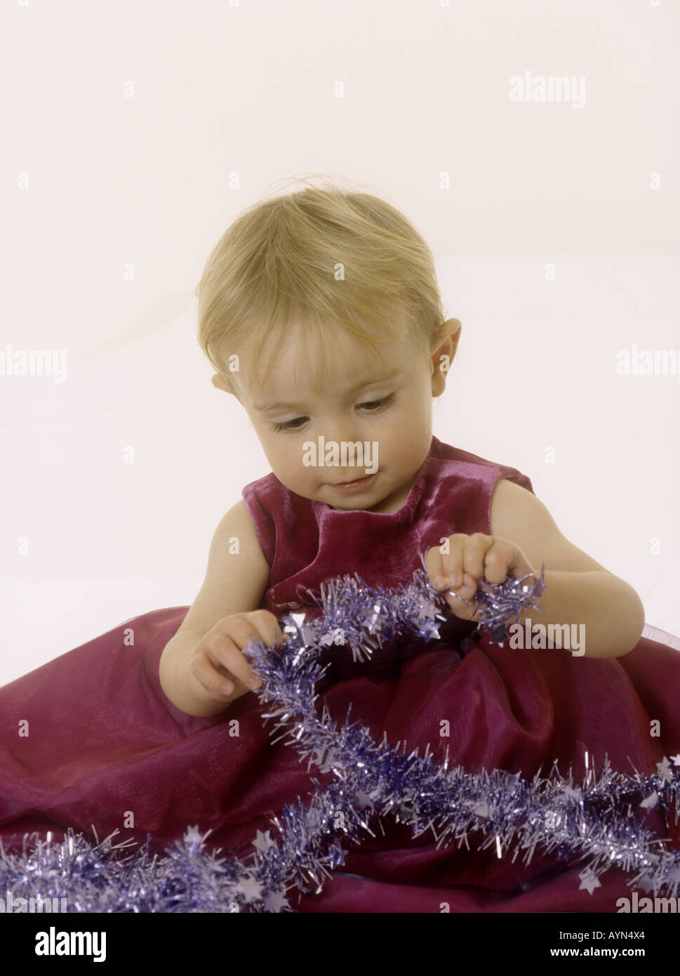 Baby girl wearing a party dress looking at tinsel at Christmas Stock Photo