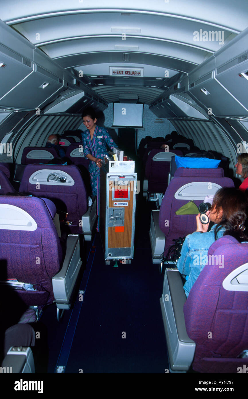 Cabin crew pushing duty free trolley down aisle through Business Class cabin on Malaysian Airlines Boeing 747 400 Stock Photo